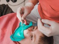The dentist treats the child's tooth using a rubber dam, the doctor looks at the tooth through a dental mirror.