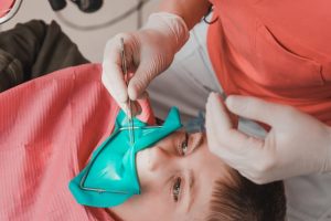 The dentist treats the child's tooth using a rubber dam, the doctor looks at the tooth through a dental mirror.